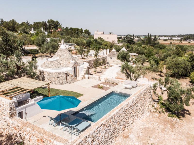 Trulli with a pool, nestled in the Apulian countryside, surrounded by olive trees and dry stone walls.