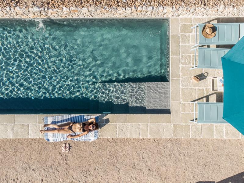 Woman sunbathing by the pool with loungers and umbrella.
