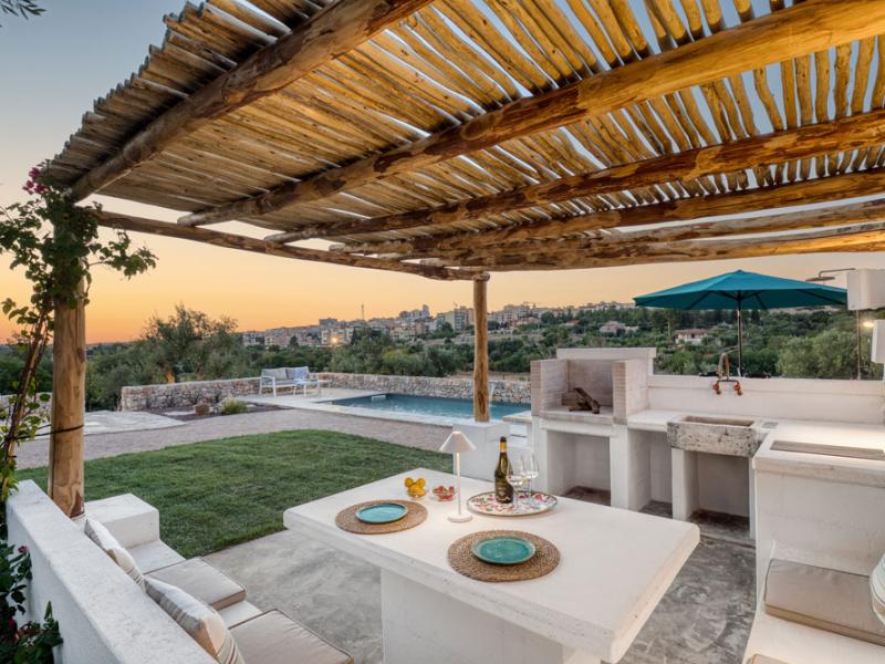Terrace with pergola, dining table, barbecue, and pool at sunset.