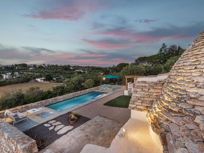 Pool with panoramic countryside view at sunset, next to a stone structure.